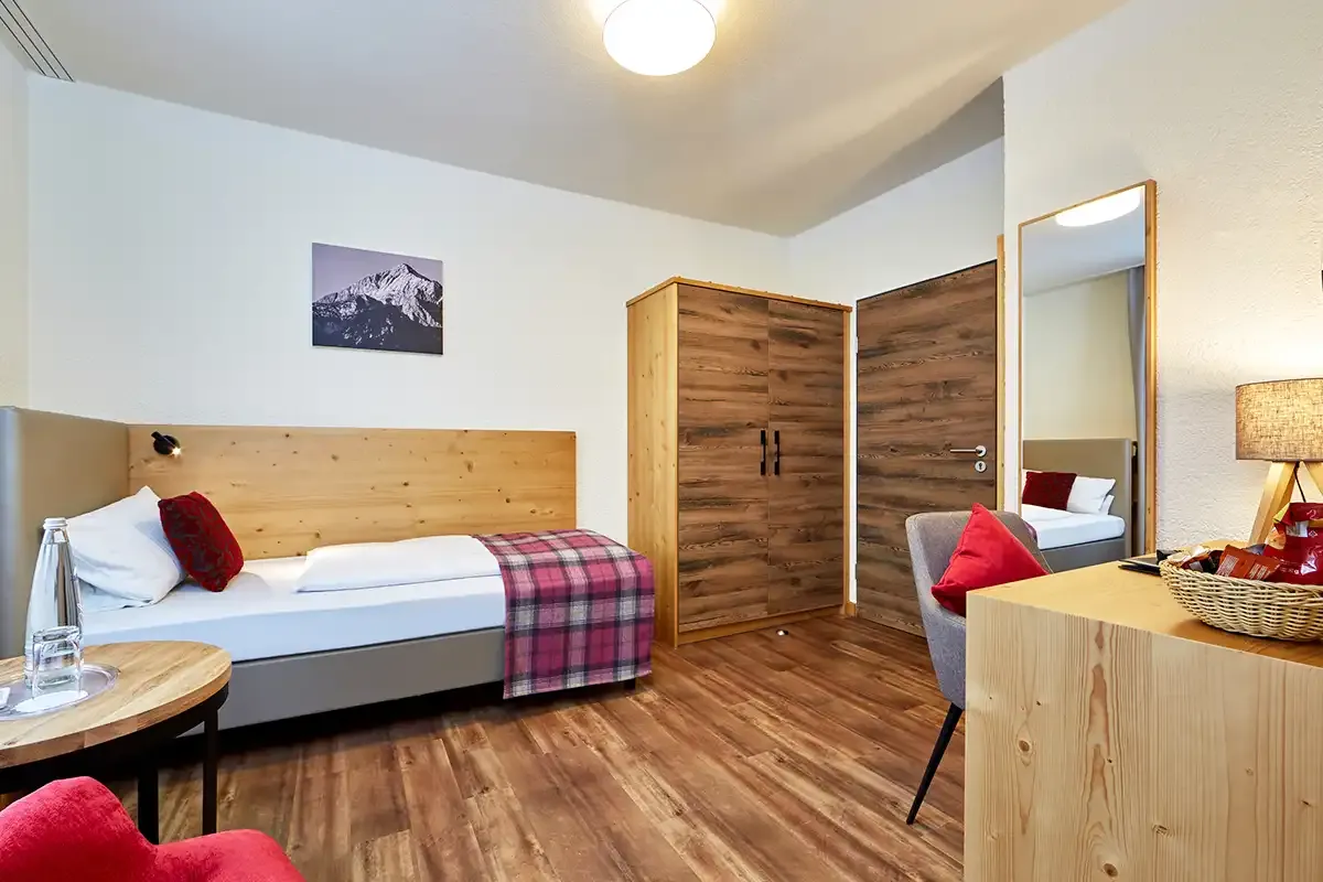 Modernes Economy-Einzelzimmmer mit Einzelbett, Kleiderschrank und Schreibtisch für einen erholsamen Urlaub.