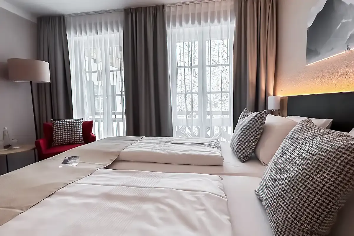Modernes Doppelbett im Hotelzimmer des Berghotel Hammersbach mit großer Fensterfront.