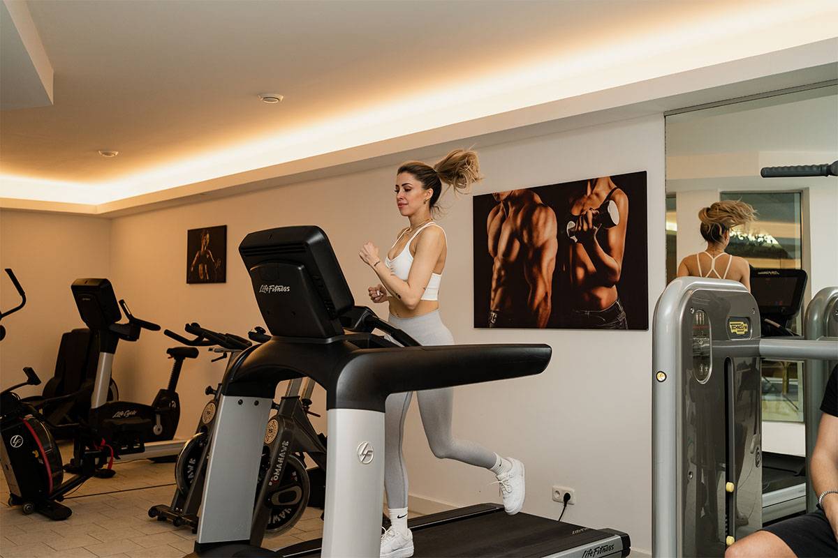 Fitnessraum im Berghotel Hammersbach mit einem Laufband, auf dem eine Frau läuft.