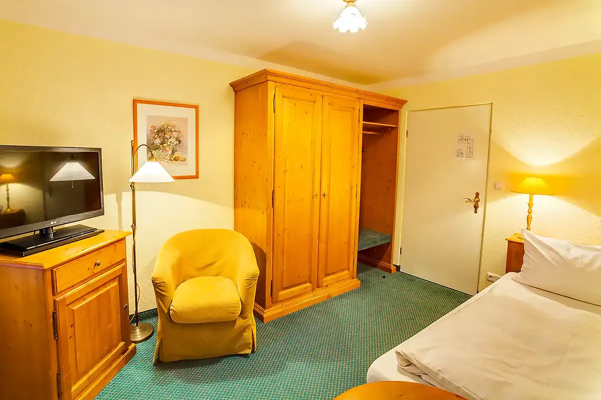 Familienzimmer mit TV, Doppelbett, Kleiderschrank und Sessel im Berghotel Hammersbach.
