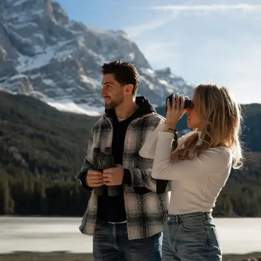 Ein Paar erkundet mit Ferngläsern in der Hand die Berglandschaft der Alpen.