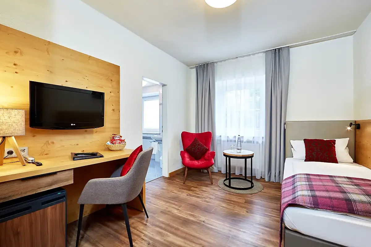 Großes Einzelzimmer mit moderner Ausstattung: Einzelbett, Schreibtisch, TV und Kühlschrank.