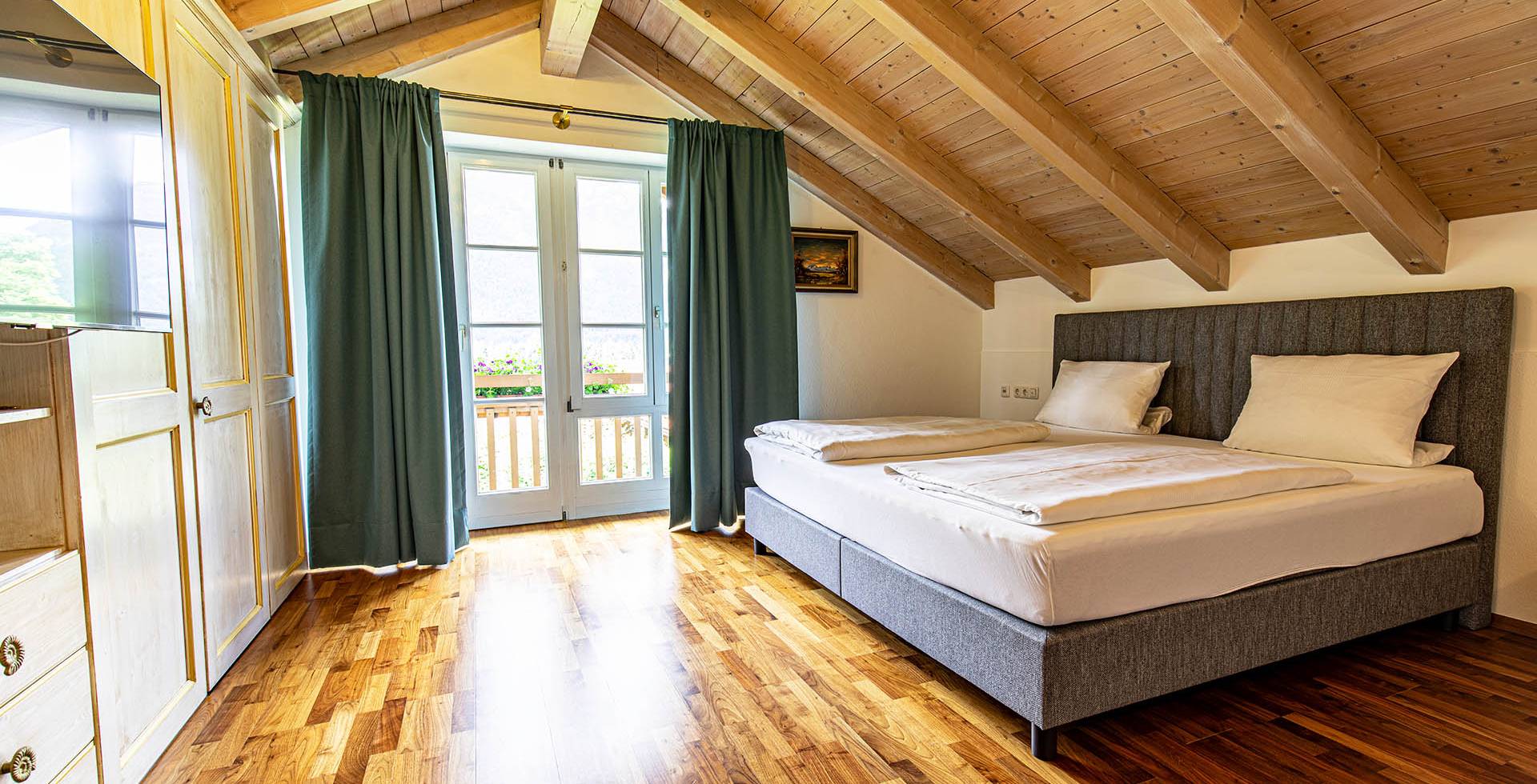 Helles Schlafzimmer im Dachgeschoss mit gemütlichem Doppelbett, TV, Kleiderschrank und Blick auf die Berge.