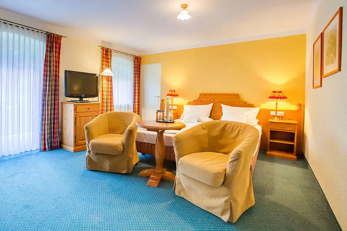 Großes Familienzimmer im Berghotel Hammersbach mit TV, Doppelbett, Sitzecke und gemütlicher Beleuchtung.