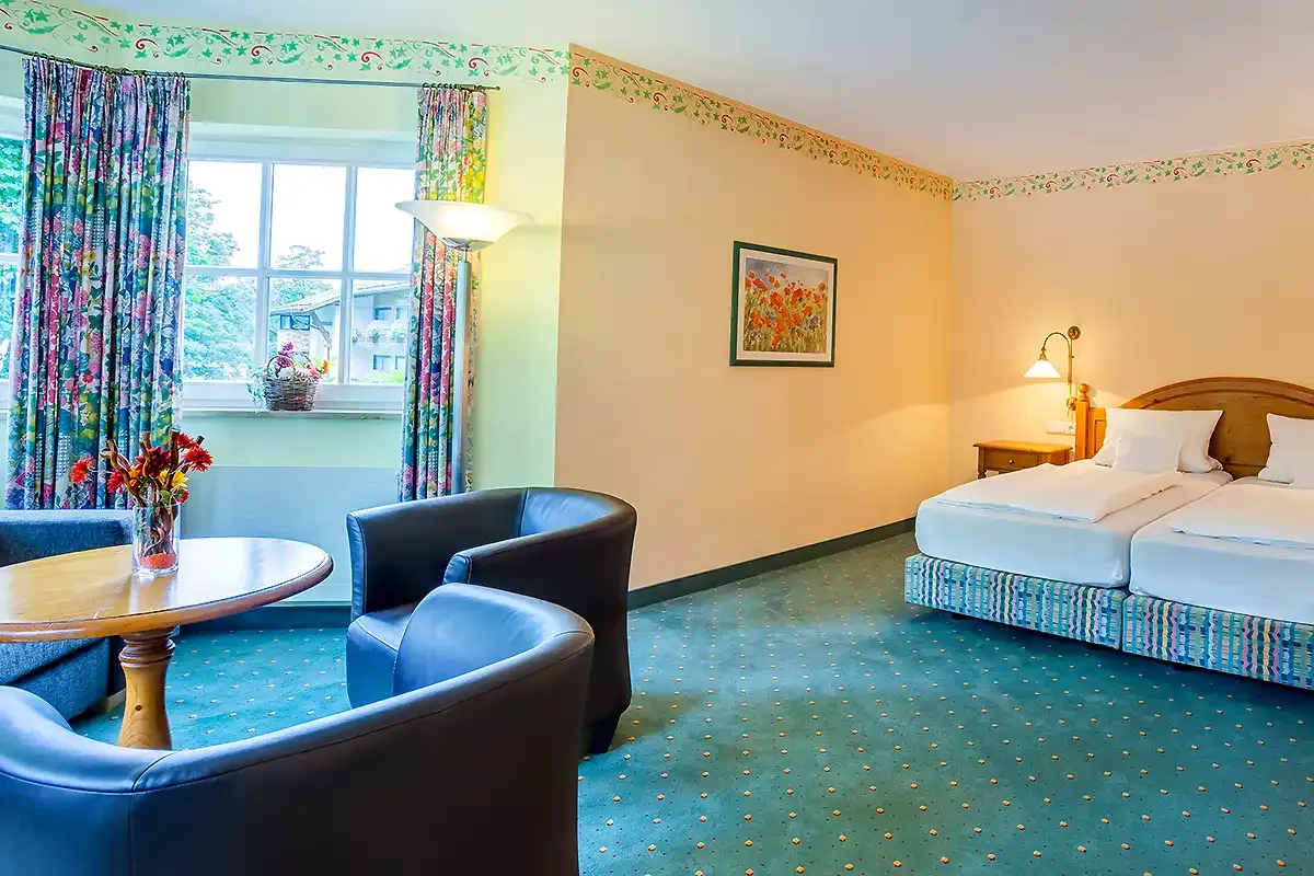 Großes Hotelzimmer mit Doppelbett im Berghotel Hammersbach und Sitzlandschaft am Fenster.