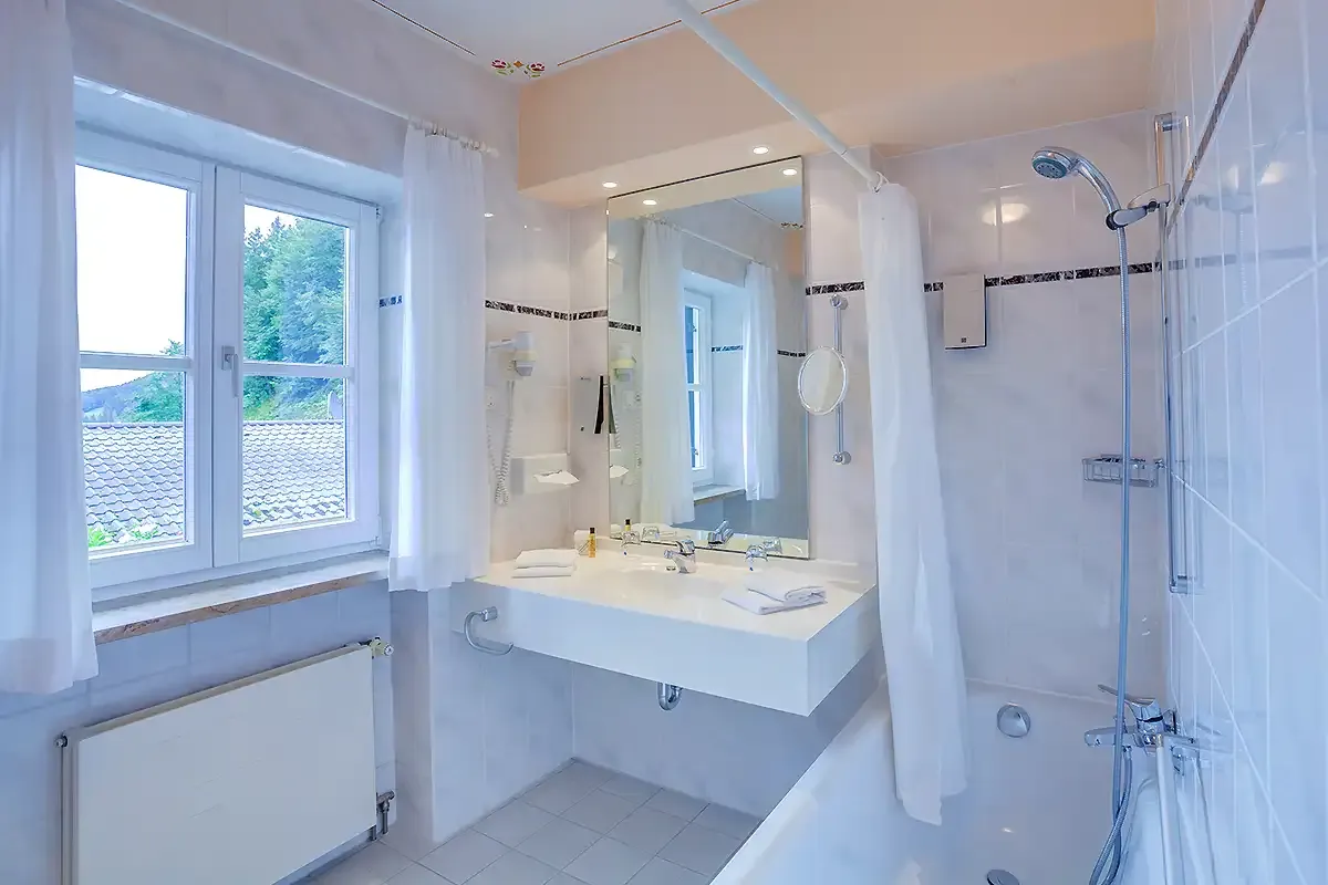 Helles Badezimmer mit Badewanne, Fenster und großen Waschtisch mit Spiegel im Berghotel Hammersbach.